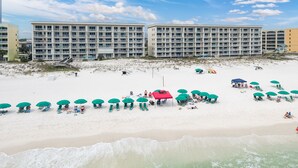 Une plage avec de nombreux parasols verts, des chaises longues et, au fond, un bâtiment doté de balcons.