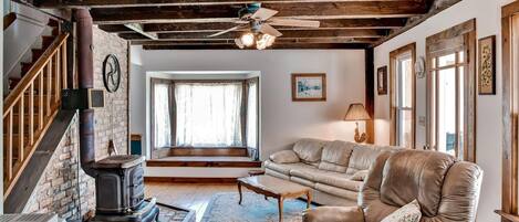 A cozy living room with exposed wooden beams, a leather sofa, a fireplace, and a staircase.