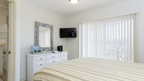 Une chambre à coucher avec un lit, une commode, un téléviseur et une fenêtre avec des stores.