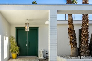 A modern building entrance with a green door, a hanging light fixture, and a potted plant.