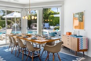 A dining area with a large table, chairs, and a view of a pool and garden.