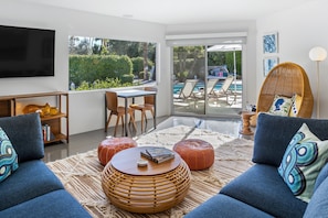 A modern living room with a TV, sofa, coffee table, and a view of a pool.