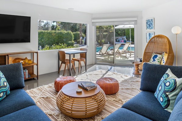 A modern living room with a TV, sofa, coffee table, and a view of a pool.