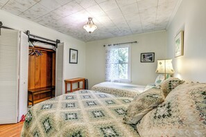 Un dormitorio con un armario de madera, una cama con colcha floral, una mesita de noche y una ventana con cortinas.