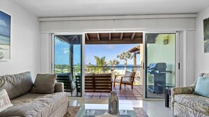 Un salón con un sofá, una alfombra estampada y una decoración con forma de estrella de mar. Hay un balcón con vistas a la playa y palmeras.