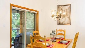 A dining area with a table set for two, a chandelier, and a window with a view of greenery. - Slope Side, Amazing Location, True Ski in & Out (Whistler)