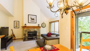 A living room with a fireplace, a sofa, a dining table with a red placemat, and a chandelier. - Slope Side, Amazing Location, True Ski in & Out (Whistler)