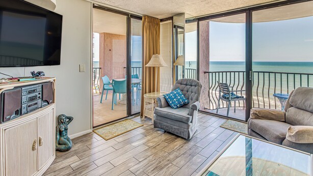 Un ampio balcone con vista sul mare, un'area salotto confortevole con divano e poltrone, e un televisore appeso al muro.
