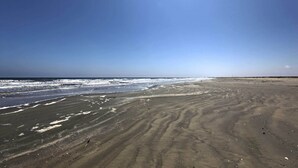 Ein Sandstrand mit sanften Wellen und blauem Himmel.