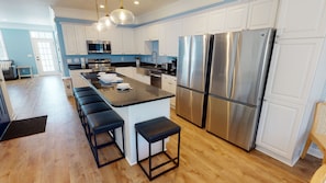 Una cocina moderna con armarios blancos, electrodomésticos de acero inoxidable, una isla central con taburetes y suelo de madera.