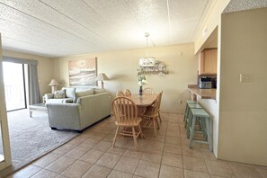 A living room with a sofa, dining table, chairs, and a kitchen area with a countertop and stools.