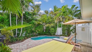 Un jardin avec une piscine, une table jaune et des chaises longues.