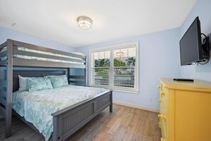 A bedroom with a bunk bed, a window with blinds, a television mounted on the wall, and a yellow dresser. - Two Bedroom Cottage with Tropical Landscaping Surrounding Private Heated Pool! (Holmes Beach)