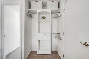 Ein weißer Schrank mit Regalen, einer Kleiderstange und einer kleinen Pflanze.