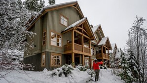 Une maison en bois à plusieurs étages, dotée d’un balcon et entourée d’arbres couverts de neige.