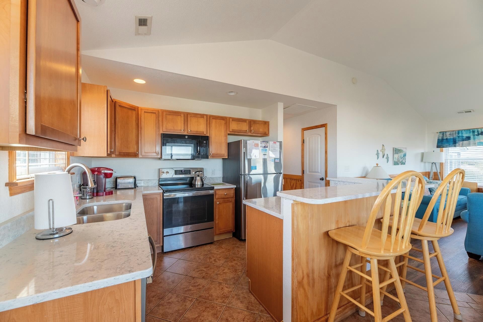A modern kitchen with wooden cabinets, stainless steel appliances, and a bar area with stools.