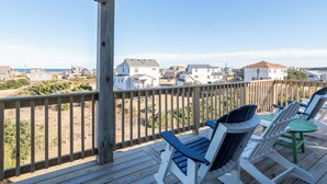 Une terrasse en bois, dotée de chaises, qui offre une vue sur une plage et un quartier résidentiel.