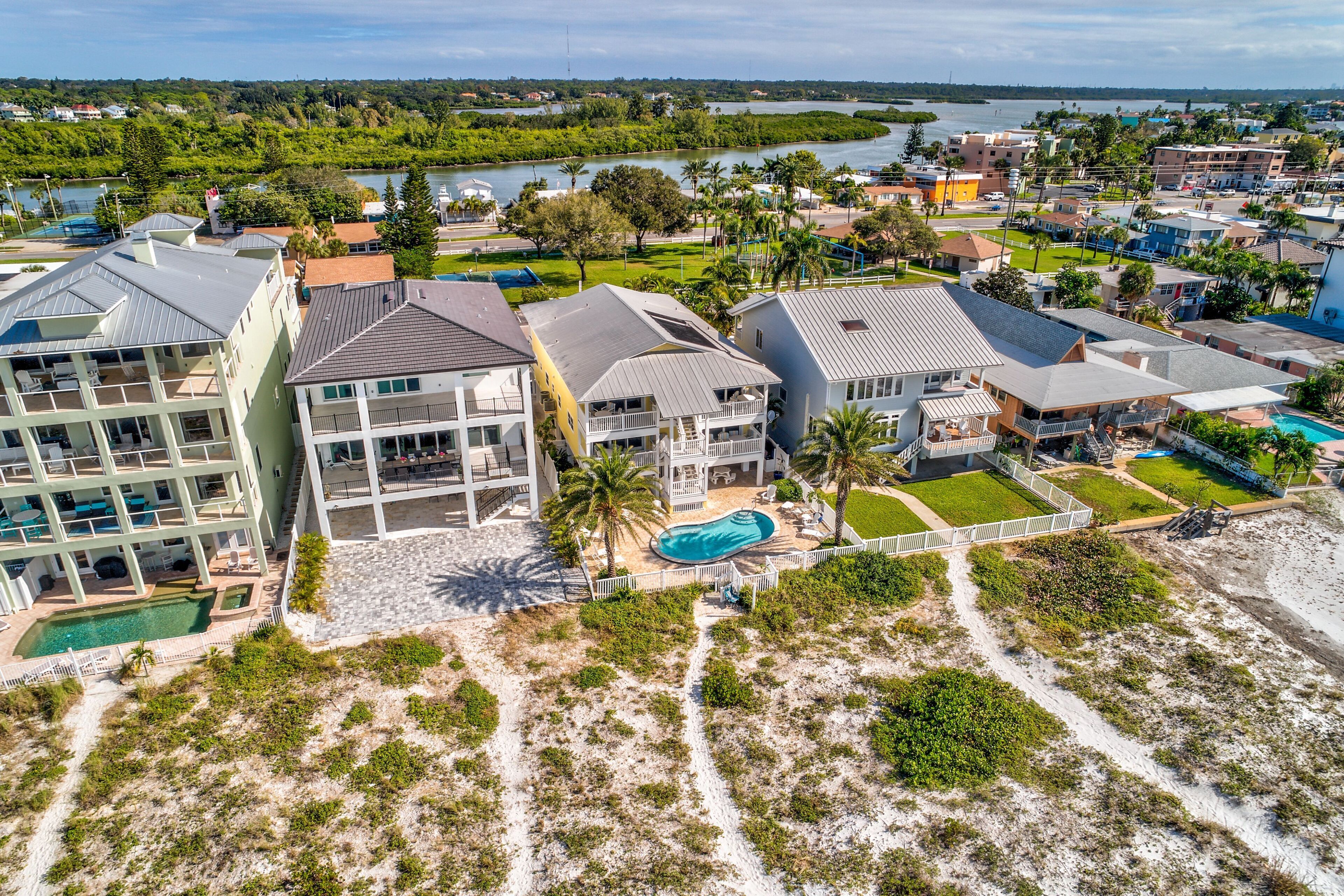 Een kustgebied met woonhuizen, meerdere tweelaagse woningen, een zwembad en een pad langs het strand.