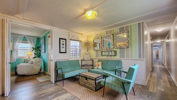 A living room with a sofa, a coffee table, a lamp, and a mirror on the wall. - The Cottage - 2 BR Beach Bungalow near Nightlife! (Surf City)
