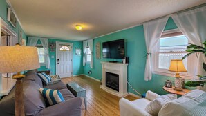 A living room with a fireplace, a television, and a sofa. - The Cottage - 2 BR Beach Bungalow near Nightlife! (Surf City)