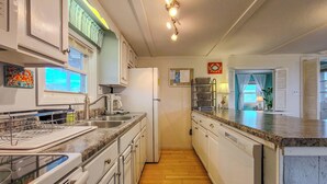 A kitchen with a stainless steel sink, white cabinets, a refrigerator, and a countertop with a coffee maker. - The Cottage - 2 BR Beach Bungalow near Nightlife! (Surf City)