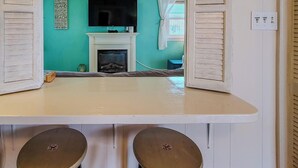 A room with a teal wall, a fireplace, a television, and a table with a lamp. - The Cottage - 2 BR Beach Bungalow near Nightlife! (Surf City)