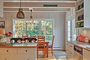 A kitchen with a dining table, chairs, a hanging light fixture, and a window with a view of trees.