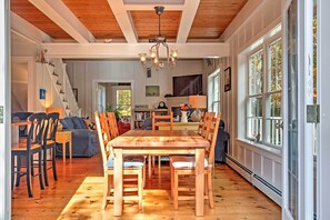 A spacious dining area with a wooden table and chairs, a chandelier, and large windows.
