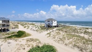 A beachfront property with a sandy path leading to a white house with a grey roof, situated on a dune. - Seaside | 6BR 4x4 OBX | Hot Tb | Sleeps 14 | 4 night stays available for fall (Carova)