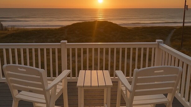 A wooden deck with two white Adirondack chairs and a small table, overlooking a sunset over the ocean. - Seaside | 6BR 4x4 OBX | Hot Tb | Sleeps 14 | 4 night stays available for fall (Carova)