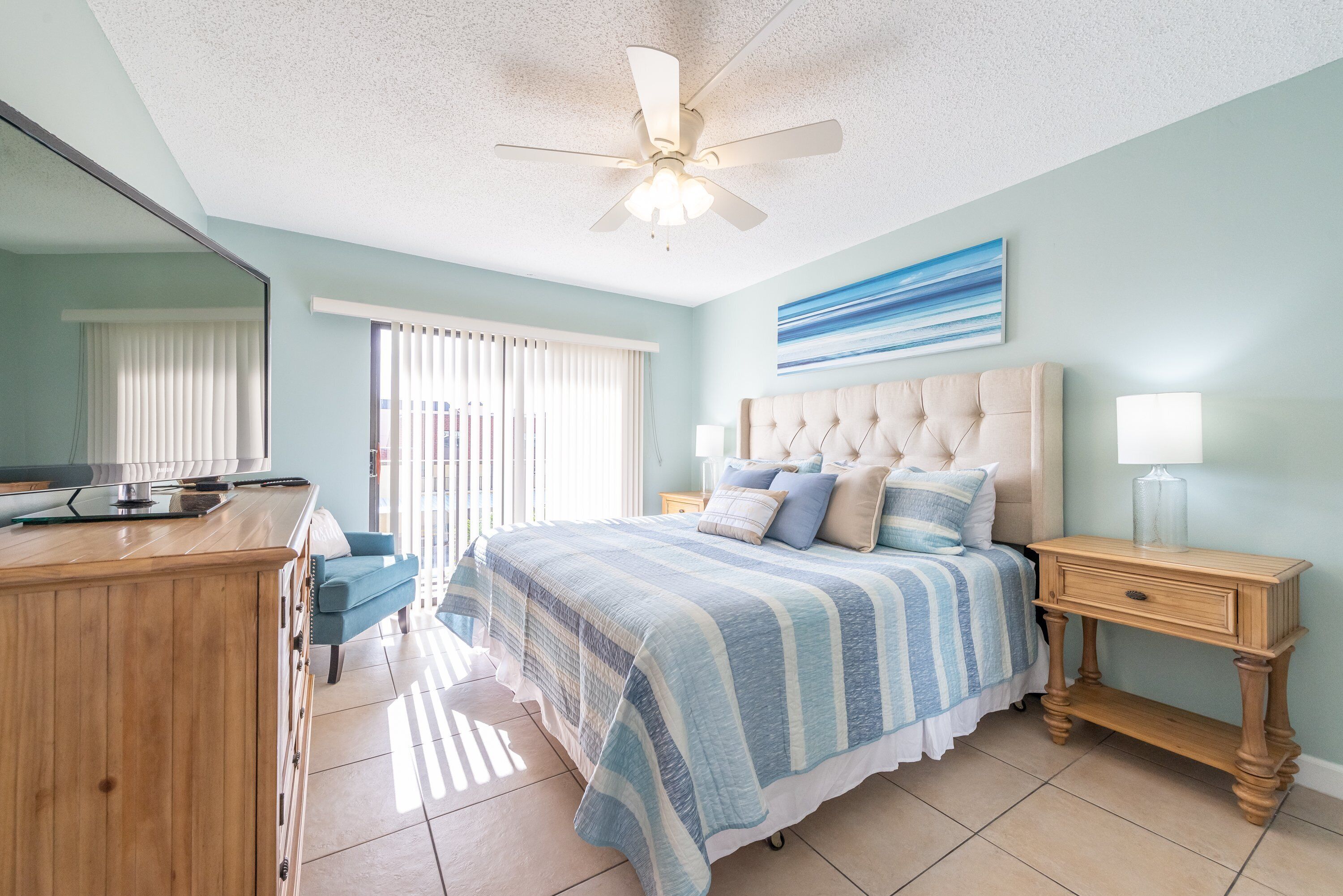 A bedroom with a bed, a nightstand, a dresser, a ceiling fan, and a window with blinds.