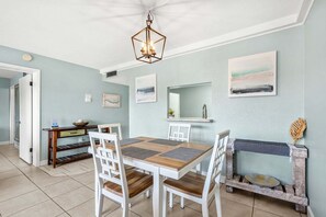 A dining area with a wooden table and white chairs, a hanging light fixture, and artwork on the walls.