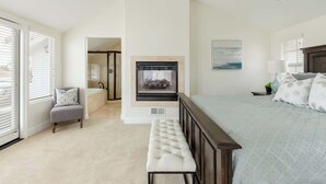 A bedroom with a large bed, a bench, a fireplace, and a bathroom visible through an open door.