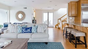 A modern living room with a sofa, a coffee table, and a kitchen area with a bar stool.