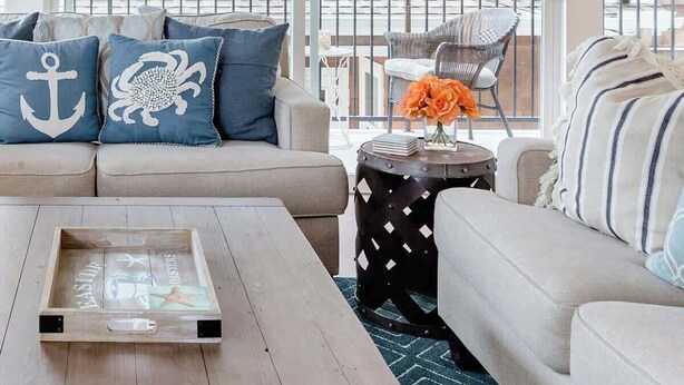A living room with a wooden coffee table, a sofa, and a chair. There is a window with a view of a wooden fence and a building.