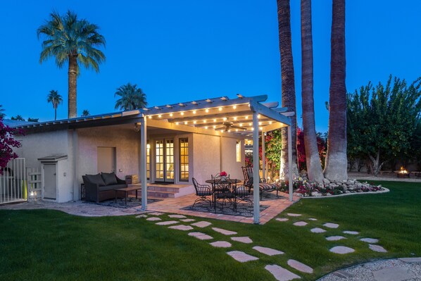 Un patio techado con mesa y sillas, un jardín pequeño y una palmera.