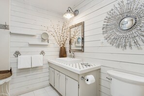A bathroom with a white vanity, a toilet, a mirror, and a decorative wall piece.