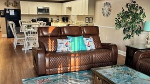 A living room with a brown leather sofa, a coffee table with a floral pattern, and a kitchen in the background.