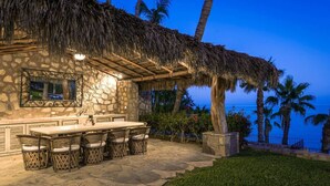 A stone building with a thatched roof, outdoor bar with seating, and a view of the ocean.