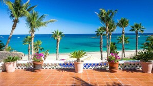 A terrace with a view of the beach and ocean, potted plants, and a white fence.
