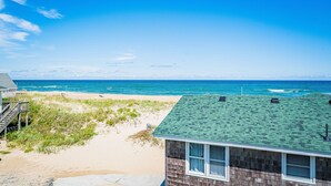 Et strandhus med grønt tag, en sandstrand og havudsigt.