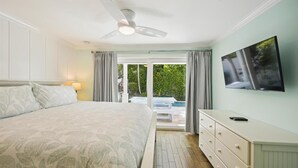 Een slaapkamer met een bed, een plafondventilator, een televisie, een dressoir en uitzicht op de omgeving.