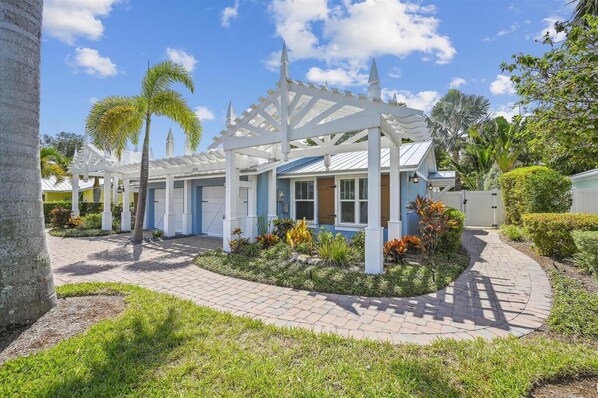 A modern house with a white porch, a blue roof, and a well-maintained garden with tropical plants.