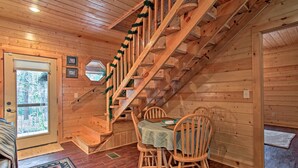 Ein Holzinterieur mit einer Treppe, einem Esstisch mit Stühlen und einem Fenster mit Jalousien.