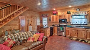 Ein gemütliches Blockhaus-Interieur mit einer Holztreppe, einem Ledersofa, einem Esstisch und einer Küchenzeile mit Holzschränken und Geräten.