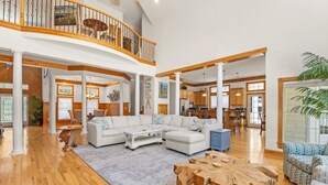A spacious living area with a large sectional sofa, wooden flooring, and a staircase leading to an upper level. - Mi Casa Bella: Private pool, hot tub, dog friendly, golf discounts & gated c (Corolla)