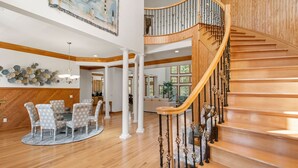 A spacious living area with a wooden staircase and a dining table with star-patterned chairs. - Mi Casa Bella: Private pool, hot tub, dog friendly, golf discounts & gated c (Corolla)