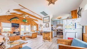 Amplia sala de estar con un televisor grande, muebles de madera y una cocina con refrigerador.