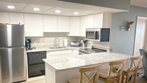 Una cocina moderna con armarios blancos, electrodomésticos de acero inoxidable y una isla central con taburetes de bar.