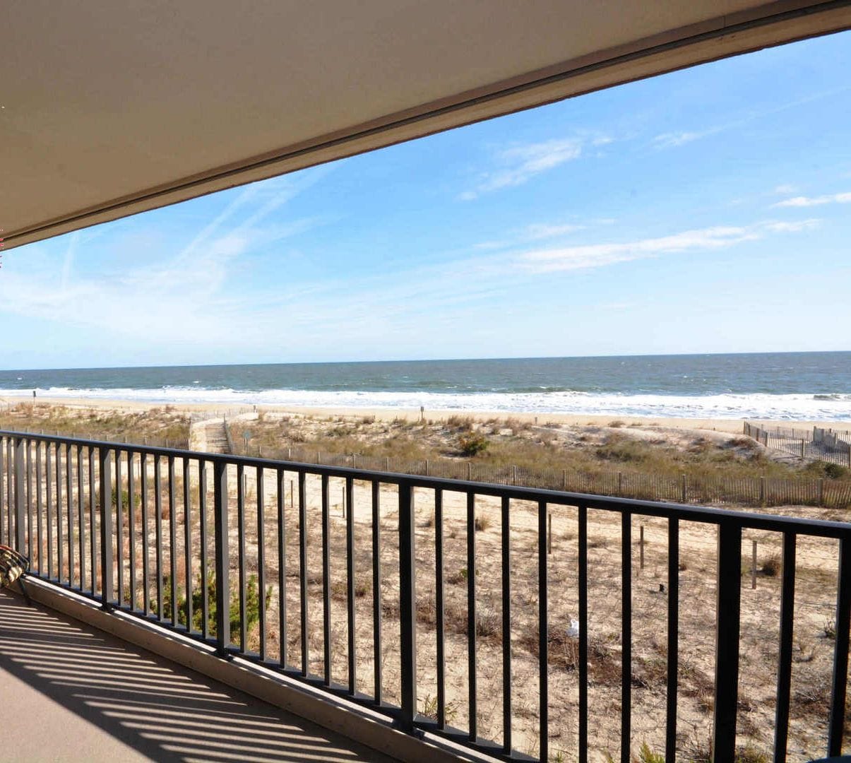 A balcony with a view of the ocean and beach, featuring a table and chairs.